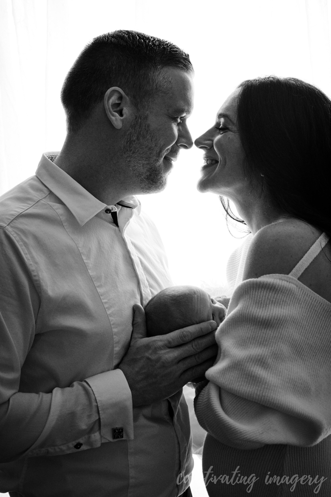 black and white image of mother and father, smiling, holding baby between them