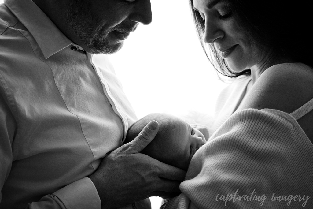 black and white image of mother and father holding baby between them