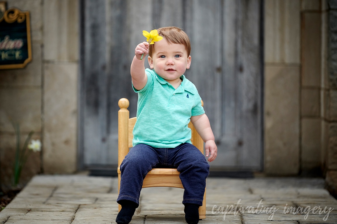 boy in chair holding up daffodil