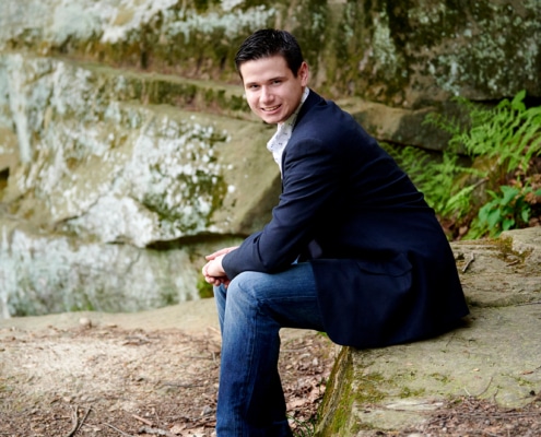 boy in suit jacket sitting under rock formation