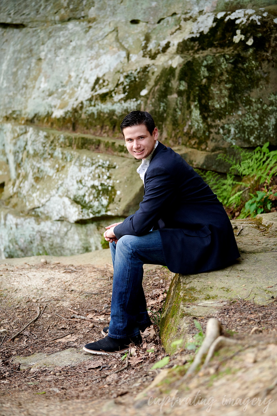 boy in suit jacket sitting under rock formation