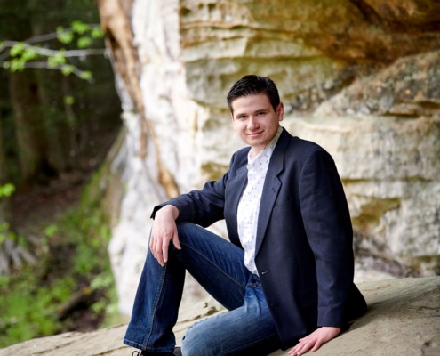 boy in suit jacket sitting under rock formation