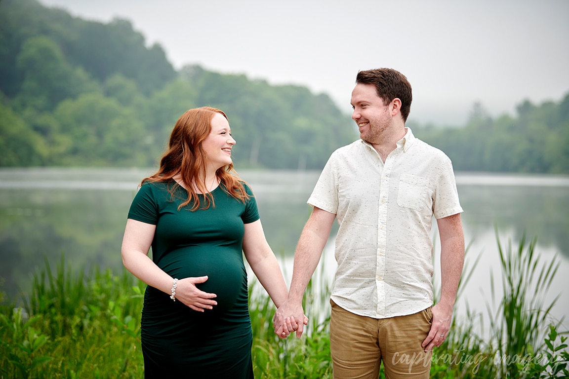 parents-to-be hold hands by lake