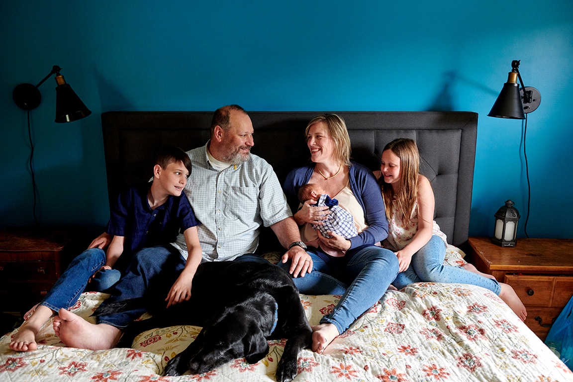 family relaxing and smiling on bed with newborn baby