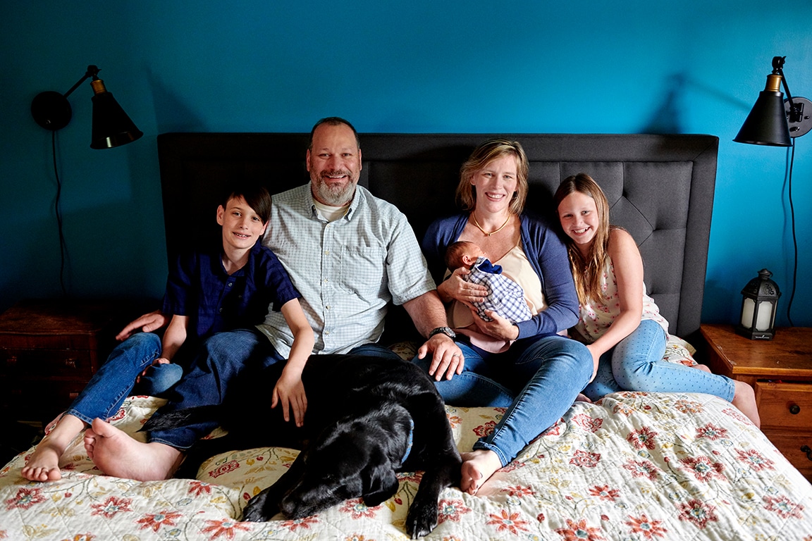 family relaxing and smiling on bed with newborn baby