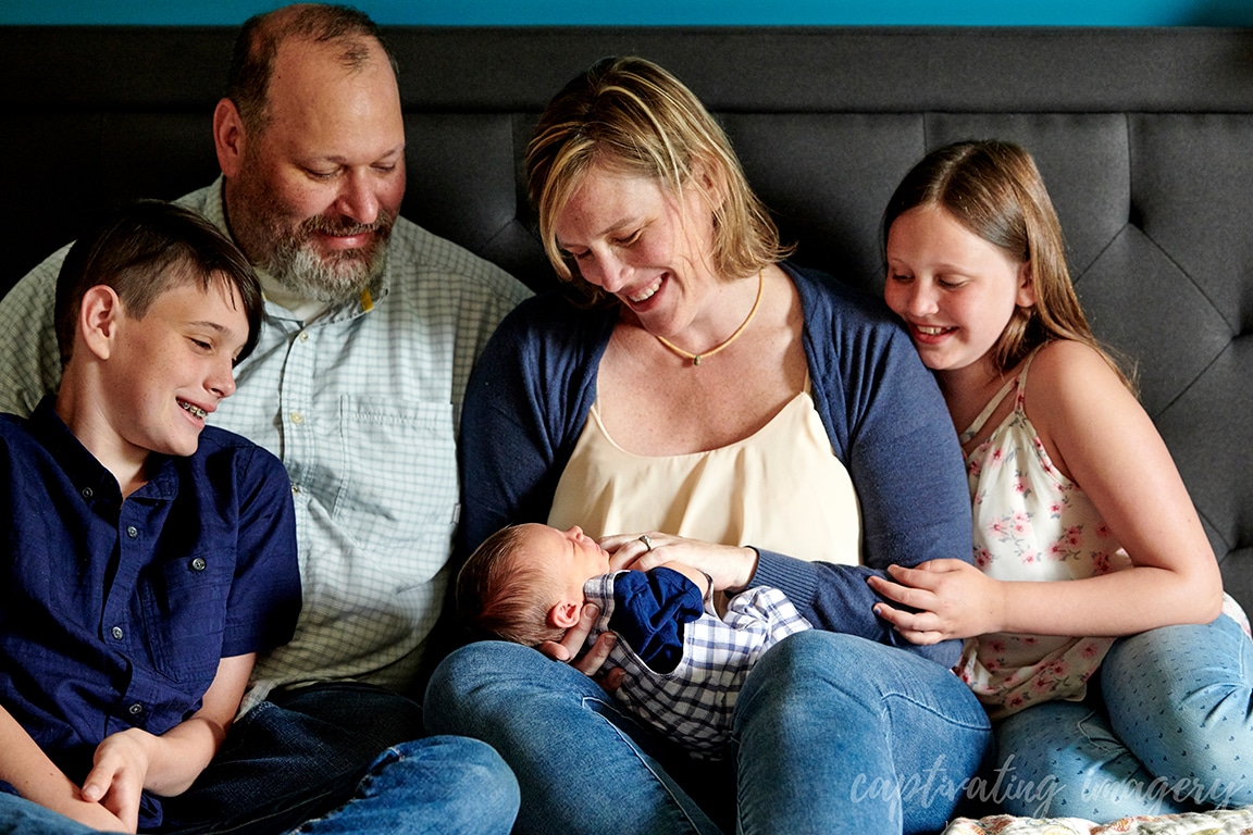 family relaxing and smiling on bed with newborn baby