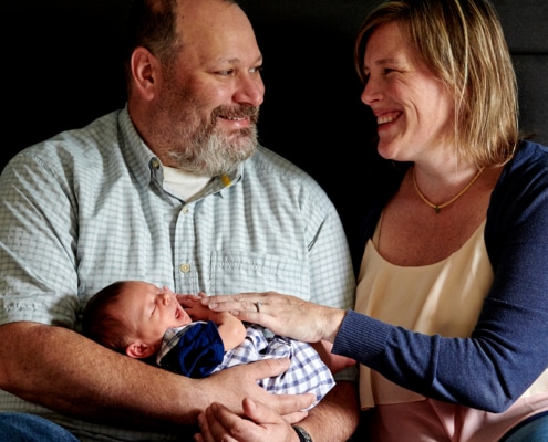 dad holds newborn with mom on bed