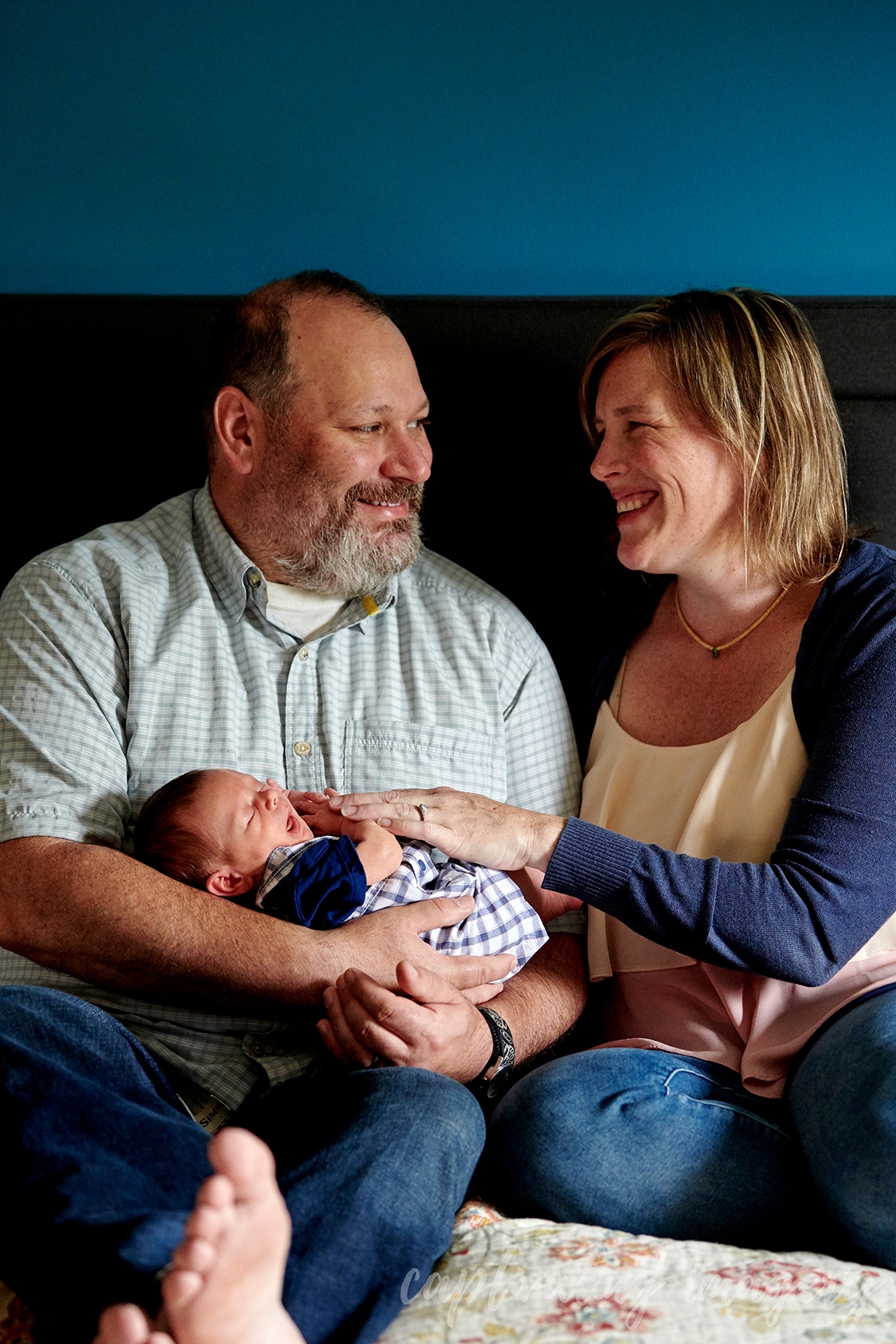 dad holds newborn with mom on bed