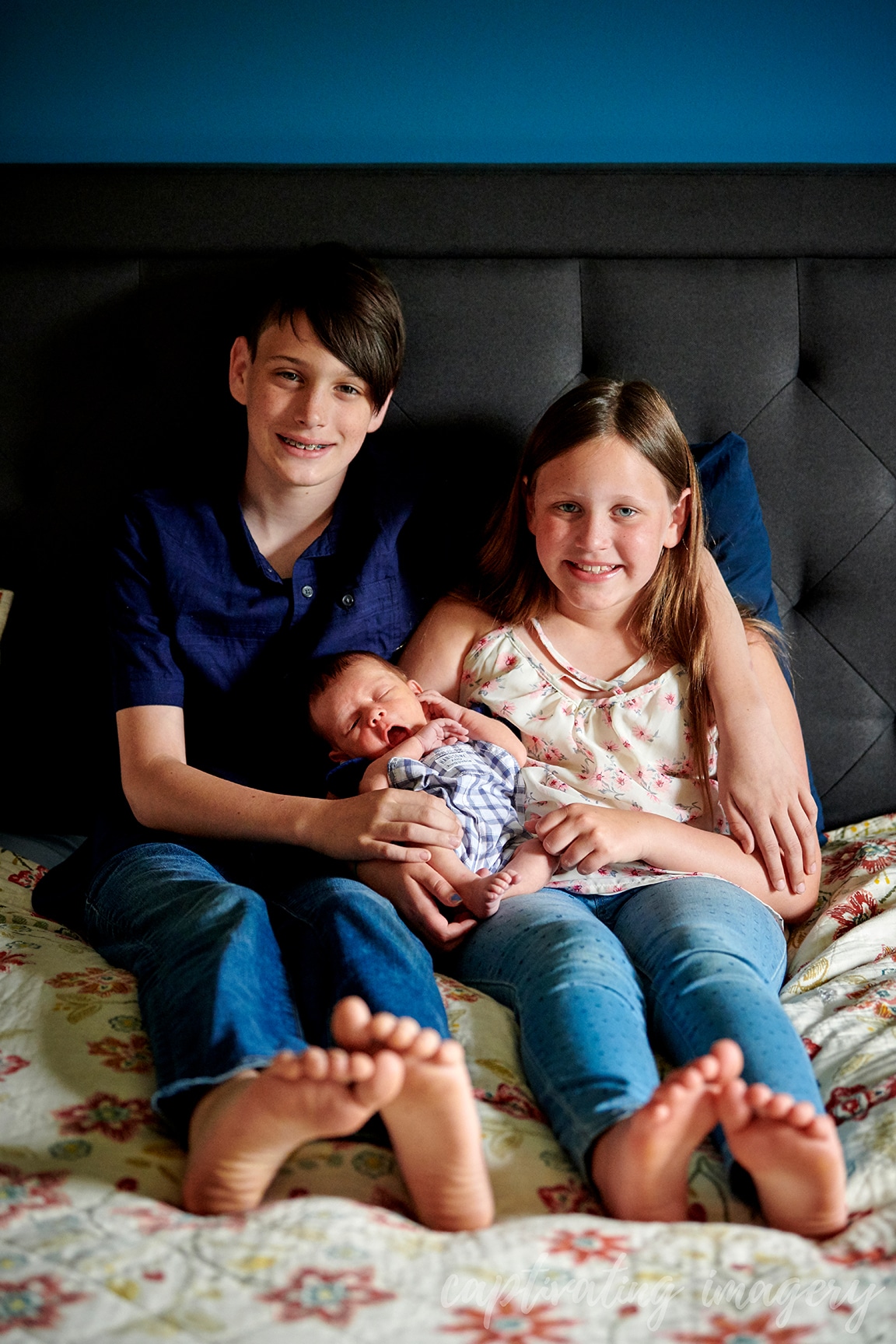 siblings hold baby on bed