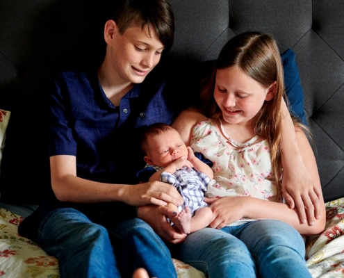 siblings hold baby on bed