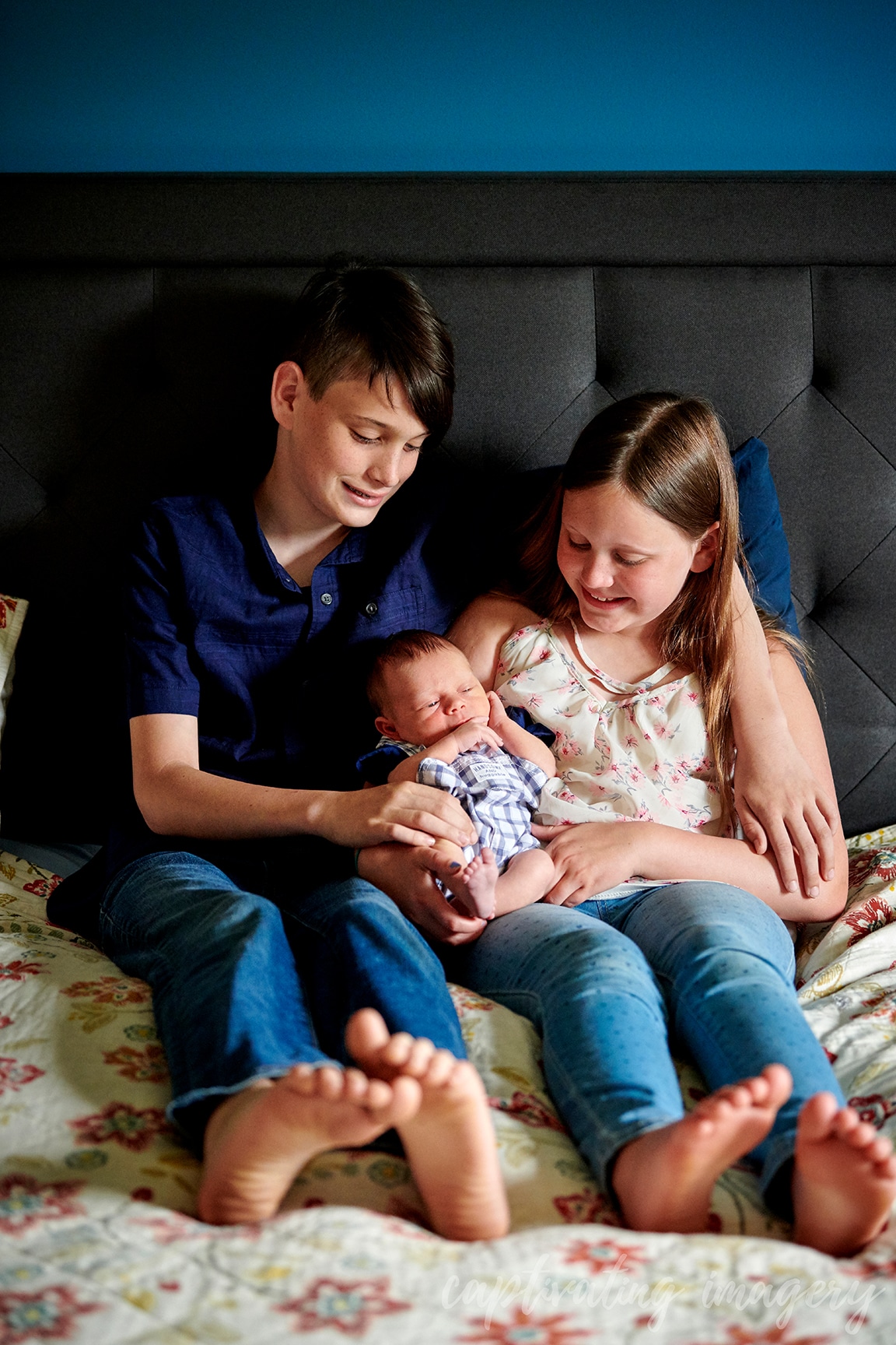 siblings hold baby on bed